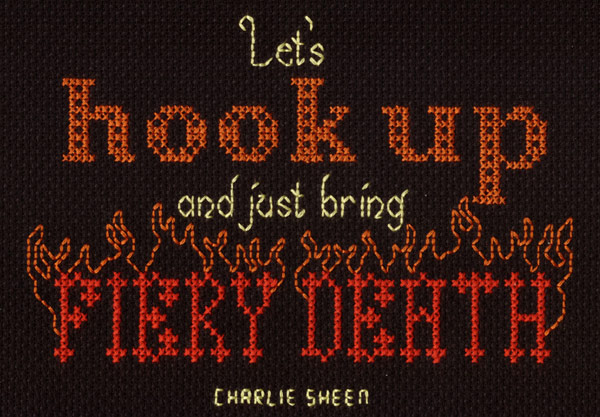 A cross stitch project that reads LET'S HOOK UP AND JUST BRING FIERY DEATH. It is a quote attributed to Charlie Sheen. It's stitched on a black piece of Aida cloth in red, orange, and yellow. The words FIERY DEATH have flames coming off them that are outlined with stitches.