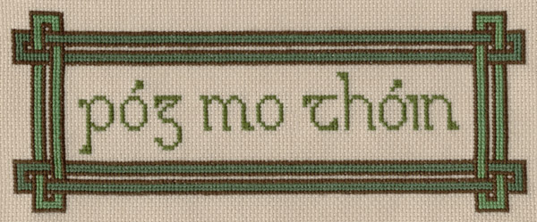 A cross stitch project on oatmeal-colored Aida cloth. It is an Irish Gaelic phrase that sounds like POUGE MOH HONE, stitched in a uncial font and framed with a simple Celtic knot border.